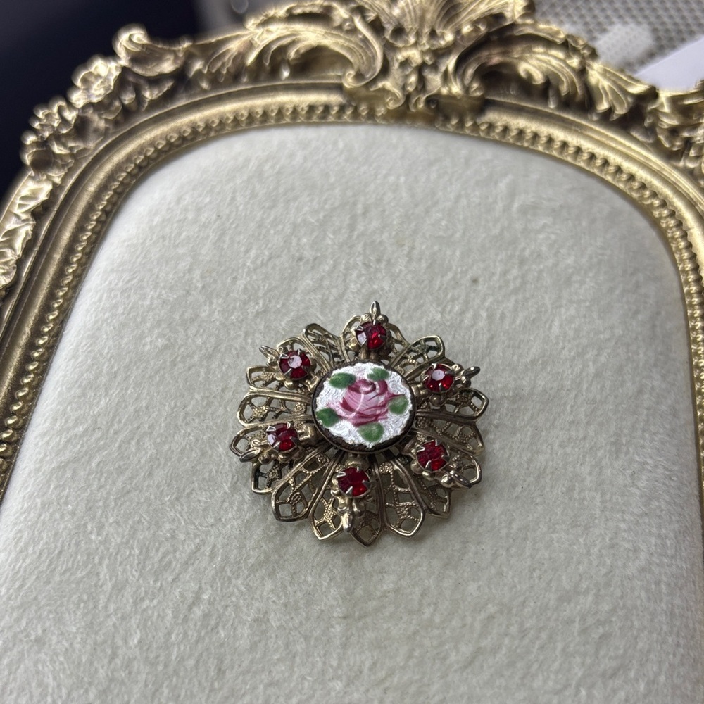 gold-tone filigree brooch with red rhinestones and a central guilloché enamel